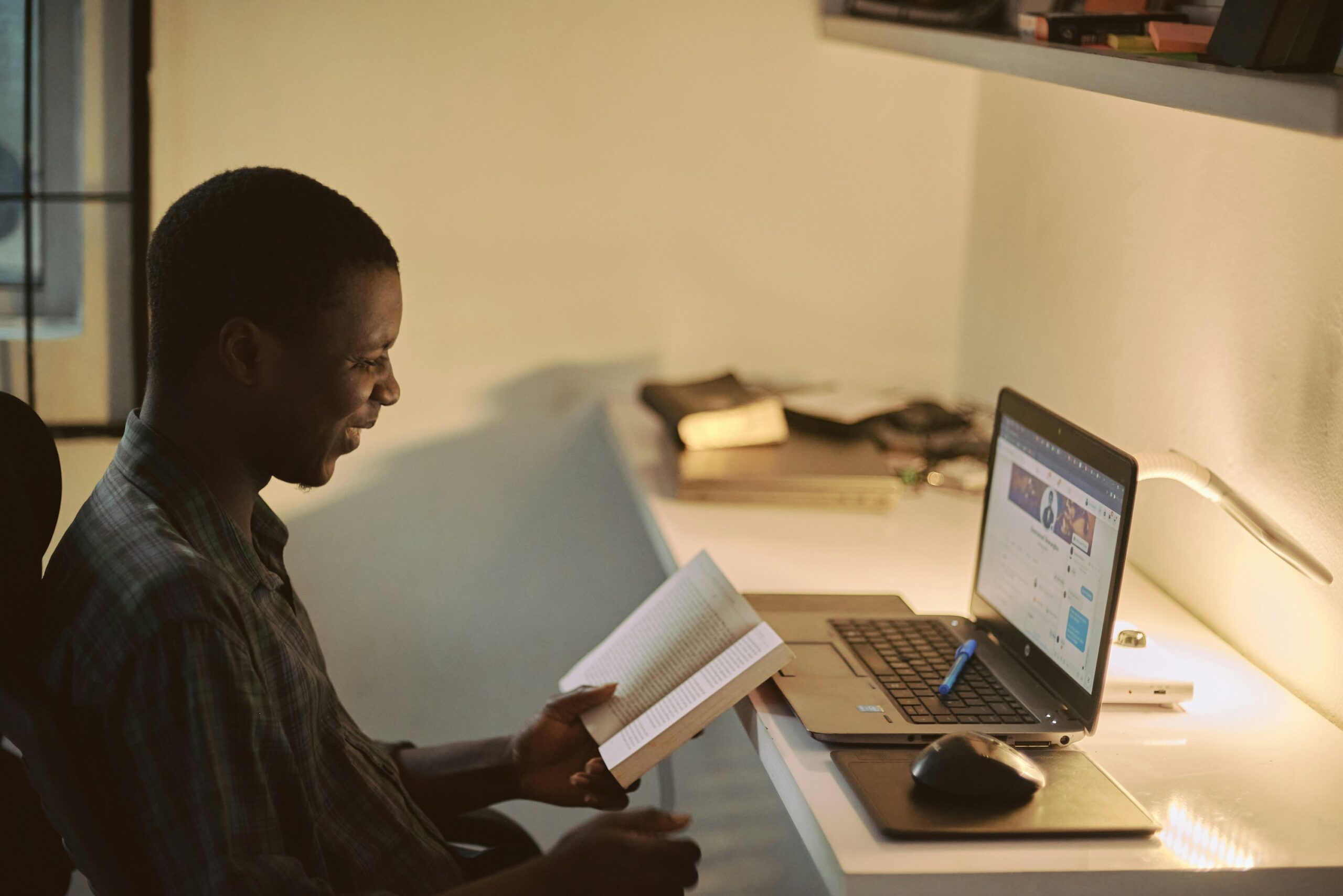 man reading a book while sitting at computer