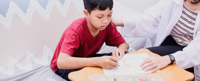 boy wearing a red shirt participating in fine motor skill exercises with a DrOT