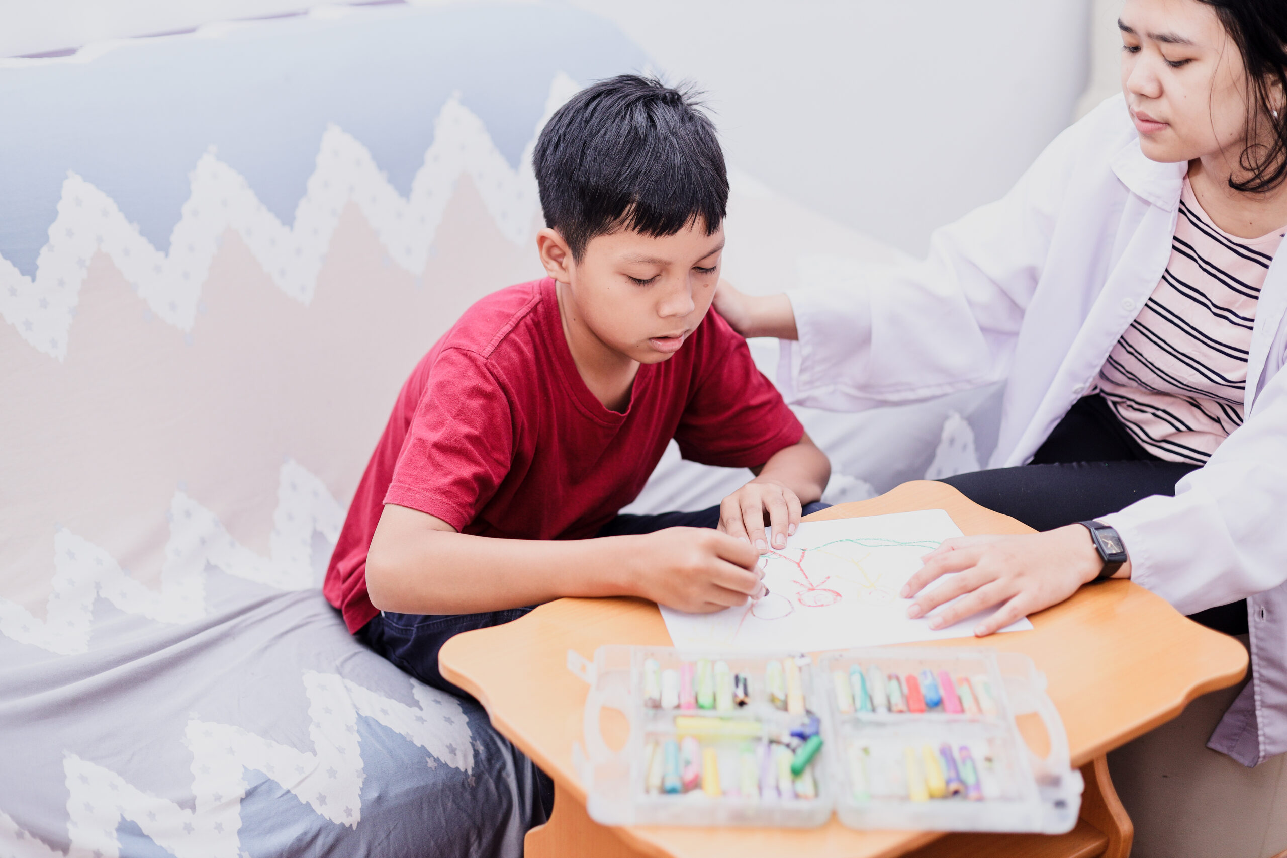 boy wearing a red shirt participating in fine motor skill exercises with a DrOT