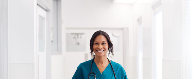 nurse wearing scrubs and smiling while walking down a hospital corridor.