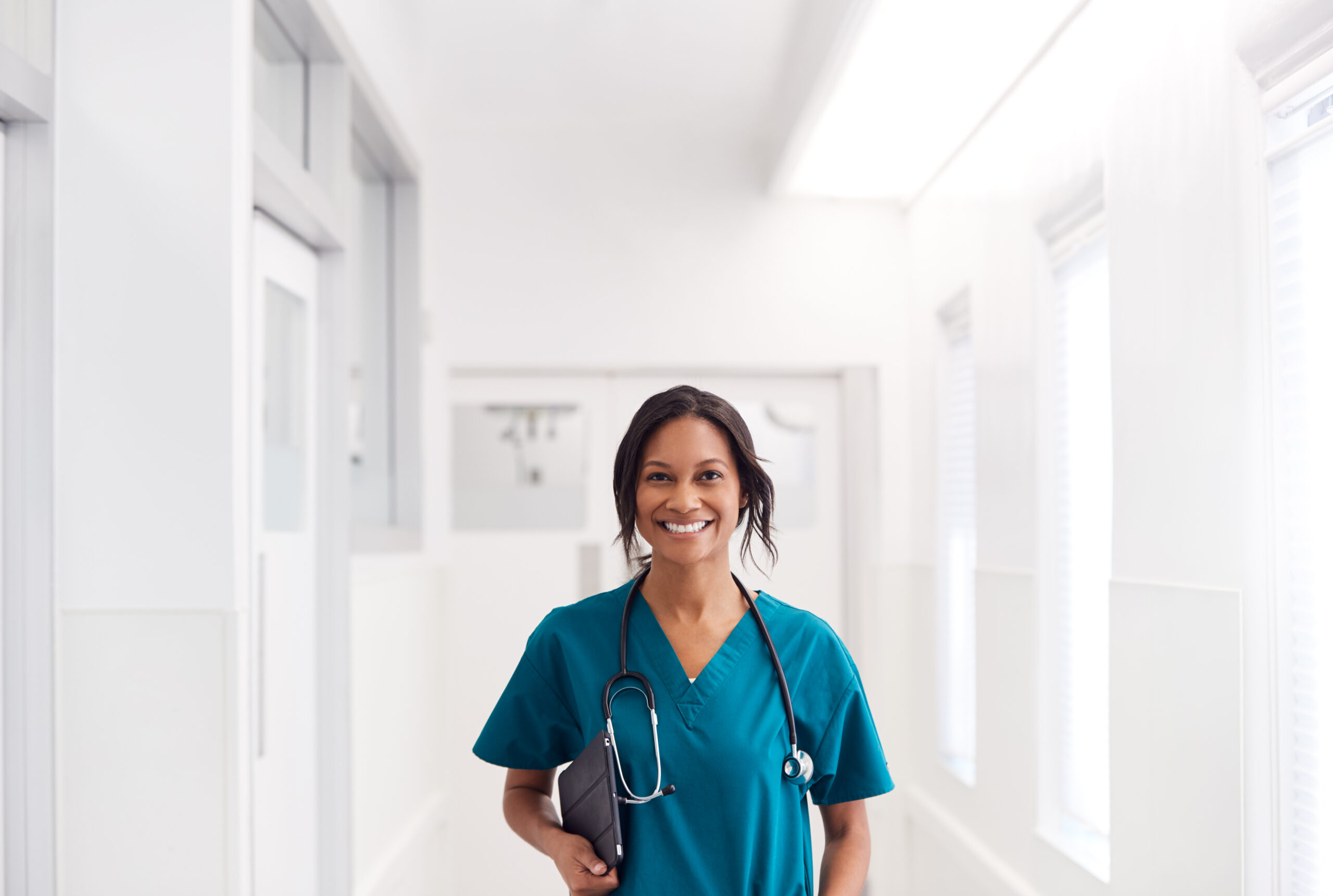 nurse wearing scrubs and smiling while walking down a hospital corridor.